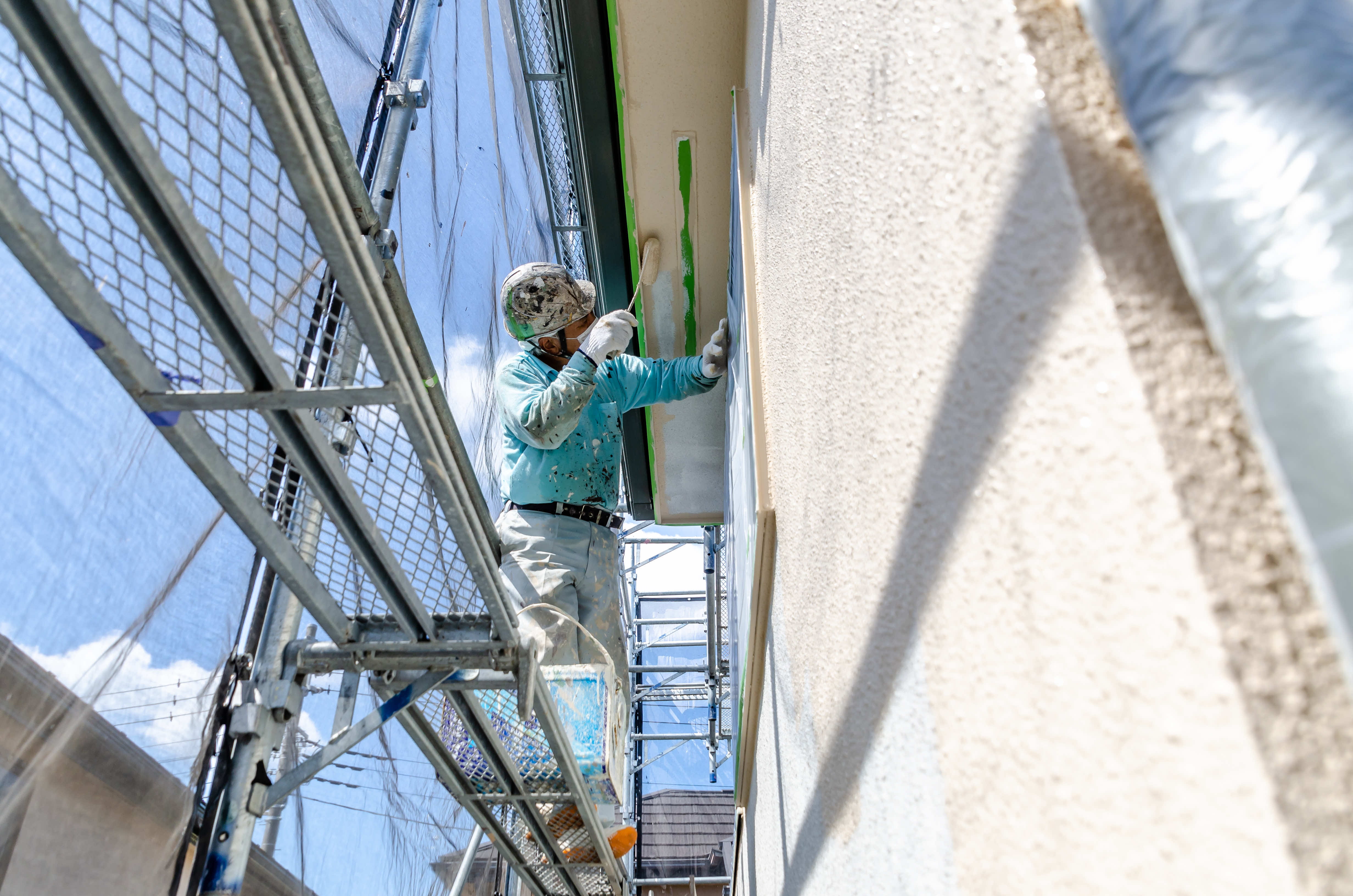 作業員が足場に立ちながら外壁を塗装している様子